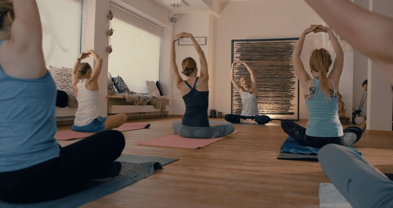 Teilnehmerinnen einer Yoga-Stunde mit erhobenen Armen im Studio
